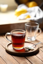 Glass cup with delicious tea and sugar on wooden table