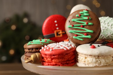 Beautifully decorated Christmas macarons on dish against blurred festive lights, closeup