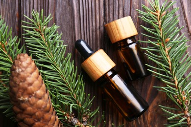 Bottles of aromatic essential oil, pine branches and cone on wooden table, flat lay