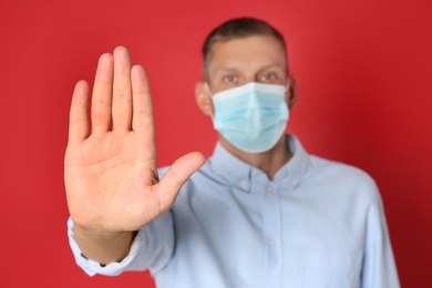 Man in protective mask showing stop gesture on red background. Prevent spreading of coronavirus