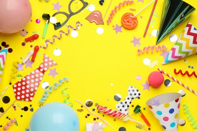 Frame of party hats and other festive items on yellow background, flat lay with space for text. Birthday surprise