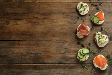 Photo of Delicious sandwiches with cream cheese and other ingredients on wooden table, flat lay. Space for text