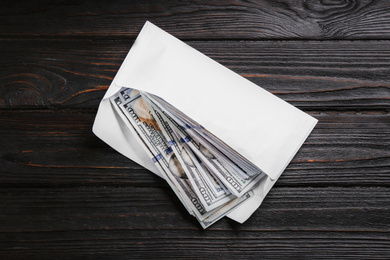 Envelope with dollar bills on black wooden table, top view. Bribe concept