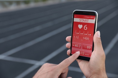 Man using fitness app on smartphone at stadium, closeup