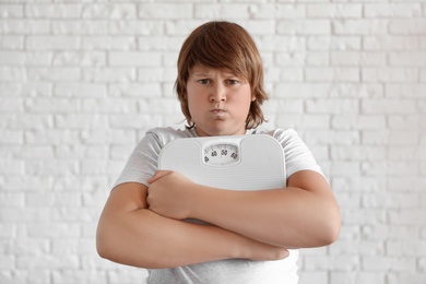 Emotional overweight boy with floor scales near white brick wall