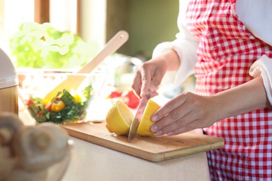 Woman cutting fresh lemon at countertop in kitchen, closeup