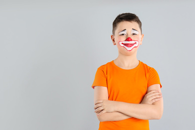 Preteen boy with clown makeup on light grey background, space for text. April fool's day