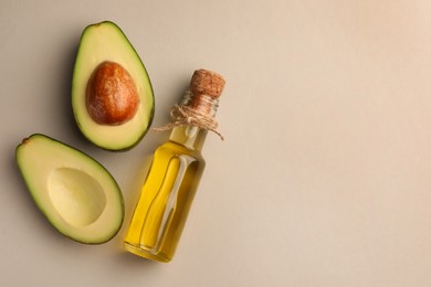 Photo of Glass bottle of cooking oil and fresh avocados on light grey background, flat lay. Space for text