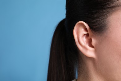 Woman on light blue background, closeup of ear. Space for text