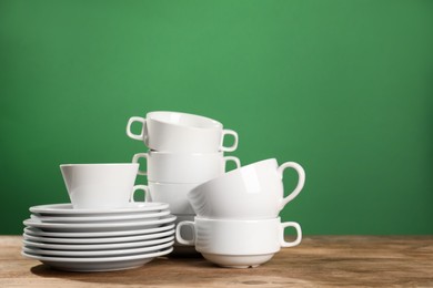 Photo of Set of clean dishware on wooden table against green background, space for text