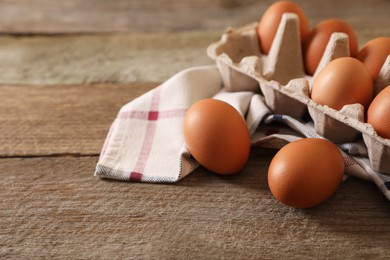Photo of Raw chicken eggs with carton and napkin on wooden table, closeup. Space for text
