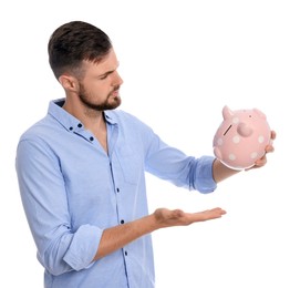 Photo of Confused young man with empty piggy bank on white background