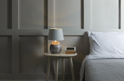 Stylish lamp, alarm clock and book on bedside table indoors. Bedroom interior elements