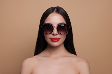 Attractive woman in fashionable sunglasses against beige background