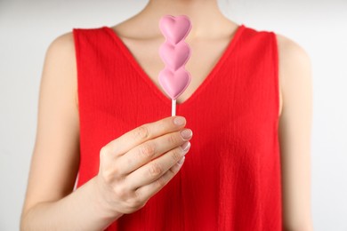 Woman holding heart shaped lollipop made of chocolate on light grey background, closeup