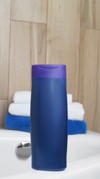 Purple bottle of bubble bath and towels on tub indoors