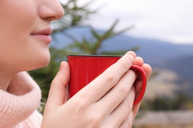 Young woman with mug of hot drink in mountains, closeup