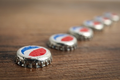 MYKOLAIV, UKRAINE - FEBRUARY 11, 2021: Pepsi lids with water drops on wooden background, closeup