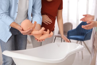 Man with pregnant wife learning how to bathe baby at courses for expectant parents indoors, closeup