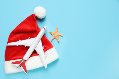 Santa hat with toy airplane, starfish and space for text on light blue background, flat lay. Christmas vacation