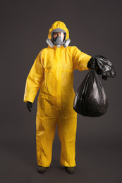 Woman in chemical protective suit holding trash bag on grey background. Virus research