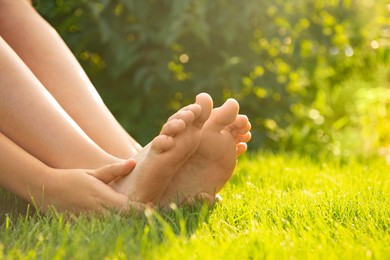 Teenage girl sitting barefoot on green grass outdoors, closeup