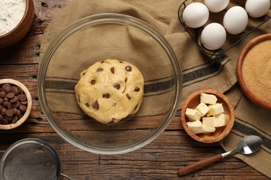 Photo of Fresh dough and different ingredients for cooking chocolate chip cookies on wooden table, flat lay
