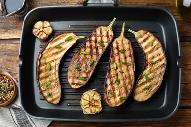 Photo of Delicious grilled eggplant halves in pan on wooden table, flat lay