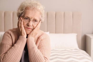 Senior woman with headache in bedroom at home. Space for text
