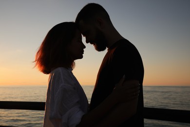 Happy young couple hugging on sea embankment at sunset