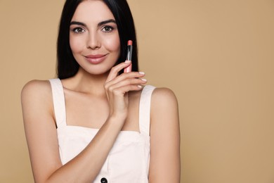 Photo of Young woman with beautiful makeup holding nude lipstick on beige background. Space for text