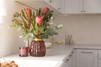 Photo of Beautiful protea flowers on countertop in kitchen, space for text. Interior design