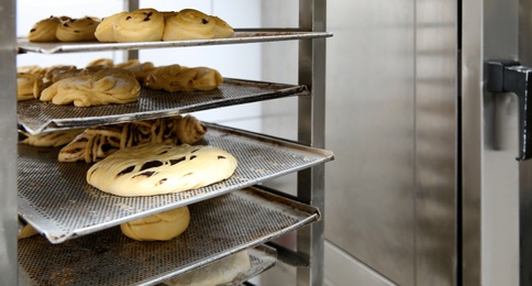 Rack with unbaked pastries in bakery workshop. Space for text