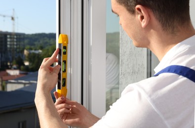 Worker using bubble level after plastic window installation indoors, closeup