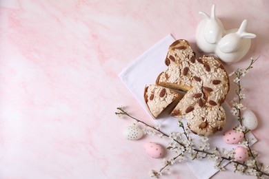 Photo of Delicious Italian Easter dove cake (traditional Colomba di Pasqua), painted eggs, figure of rabbits and branches with flowers on pink marble table, flat lay. Space for text