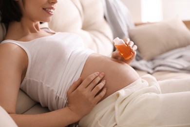Young pregnant woman with cosmetic product on sofa indoors, closeup
