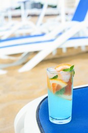 Photo of Glass of refreshing drink with grapefruit and mint on blue lounger at beach, space for text