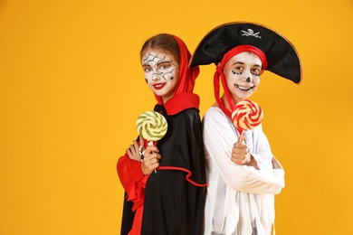 Cute little kids with lollipops wearing Halloween costumes on yellow background