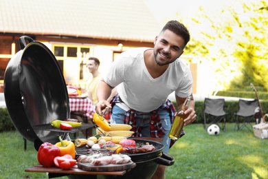 Photo of Young man with beer cooking on barbecue grill outdoors