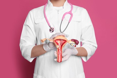 Doctor demonstrating model of female reproductive system on pink background, closeup. Gynecological care