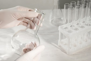 Scientist holding empty flask at white table, closeup