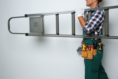 Professional builder carrying metal ladder on light background, closeup