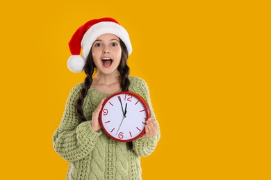 Girl in Santa hat with clock on yellow background, space for text. New Year countdown