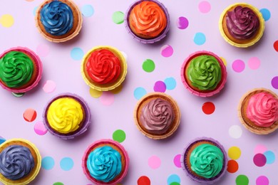 Many delicious colorful cupcakes and confetti on violet background, flat lay