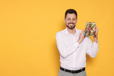 Happy man with gift box on yellow background, space for text