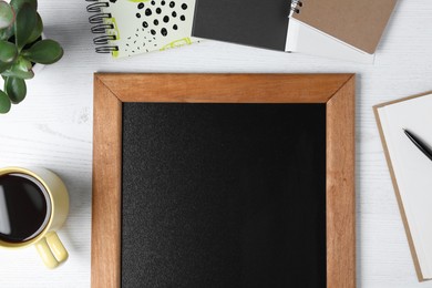 Clean small chalkboard, coffee, plant and stationery on white wooden table, flat lay