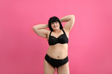 Beautiful overweight woman in black underwear on pink background. Plus-size model