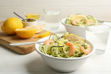 Delicious zucchini pasta with shrimps and lemon in bowl served on white wooden table