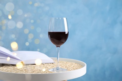 Glass of red wine and open book on white table against light blue background, space for text