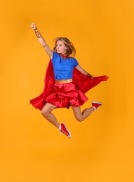 Confident woman in superhero costume jumping on yellow background